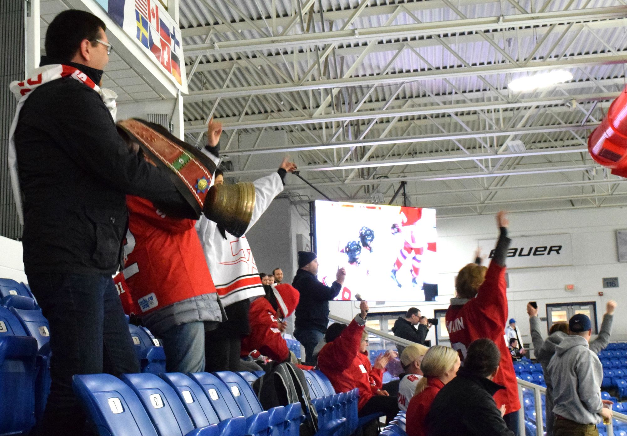 Swiss supporters at the Women's Worlds in Plymouth in 2017. Many people in red are standing and cheering but the foreground of the photograph shows a person with a large brass-colored bell swinging it around.